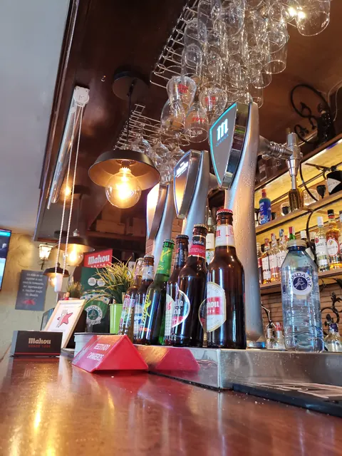 Barra de madera de Sidrería El Gallu con copas colgadas, grifos y lámpara de forja