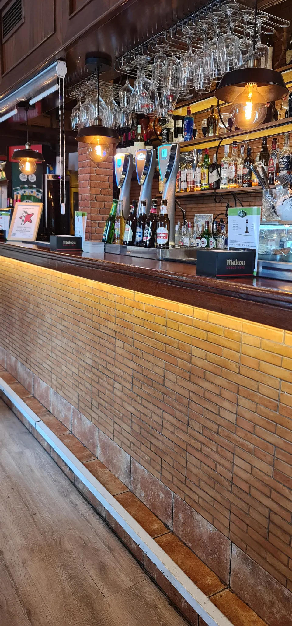 Barra de madera iluminada con botellero y copas en Sidrería El Gallu