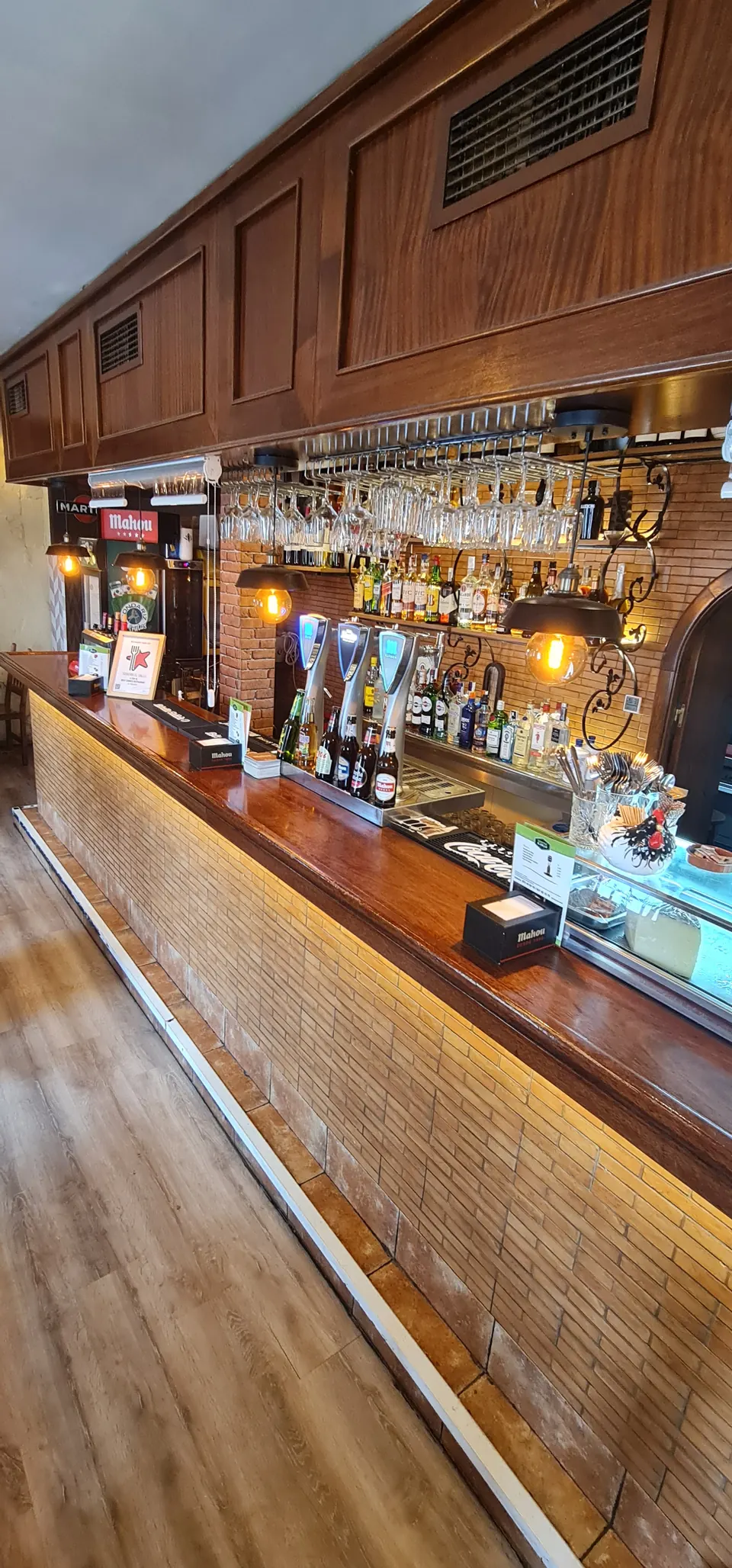Barra larga de la sidrería en Móstoles iluminada, con taburetes de madera