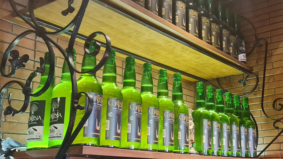 Botellas verdes de sidra natural en el botellero de forja de Sidrería El Gallu, en Móstoles