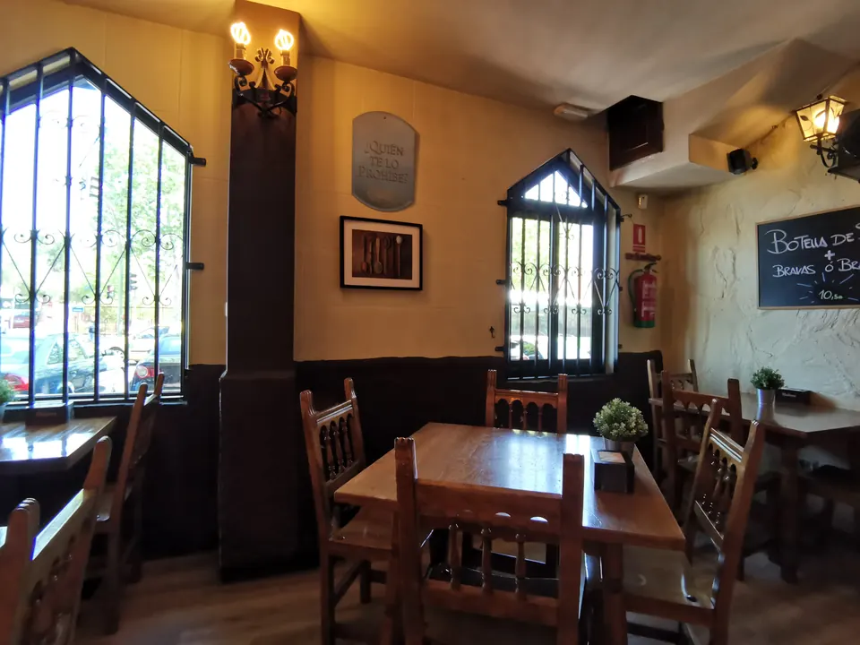 Salón de la sidrería asturiana con mesas y sillas de madera y ventanas con reja